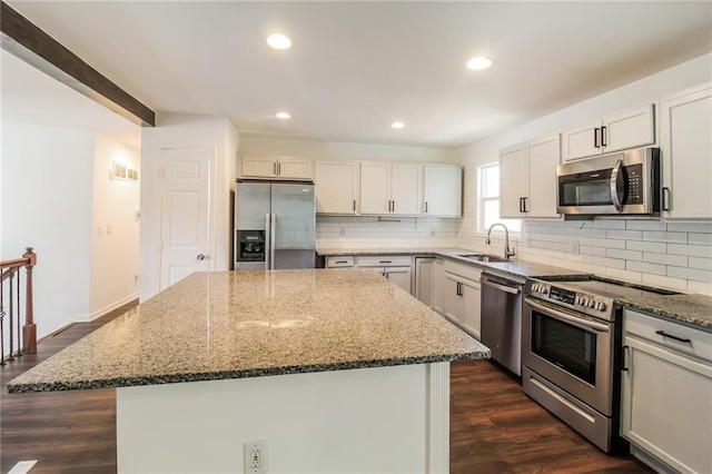 kitchen with stone countertops, a sink, a kitchen island, stainless steel appliances, and decorative backsplash