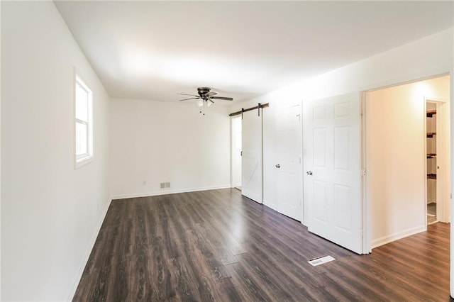 interior space with visible vents, a ceiling fan, a barn door, baseboards, and dark wood-style flooring