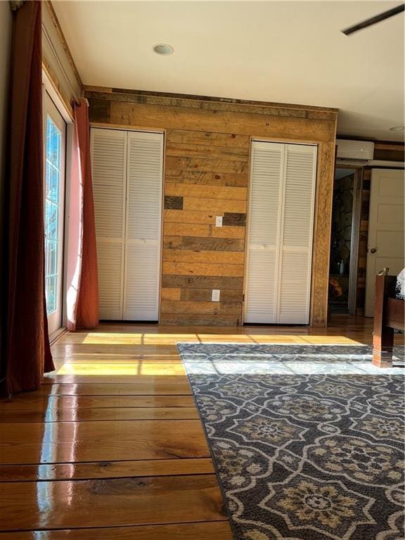 unfurnished bedroom with multiple closets, hardwood / wood-style flooring, an AC wall unit, and wood walls