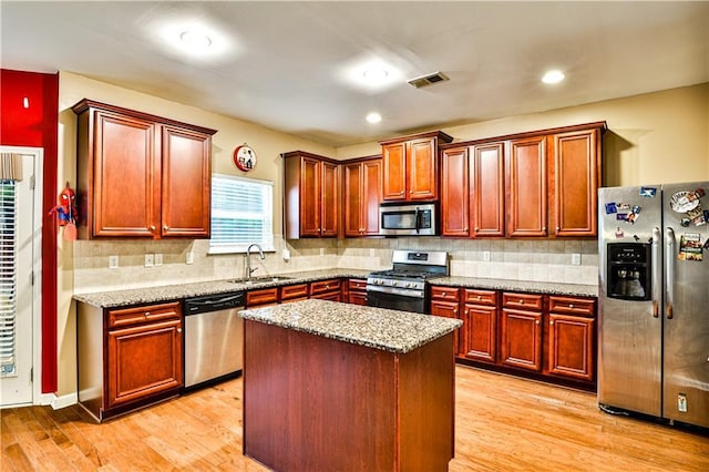 kitchen with sink, appliances with stainless steel finishes, a center island, light stone counters, and light wood-type flooring