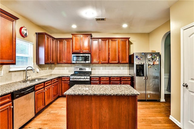 kitchen featuring sink, stainless steel appliances, light stone countertops, a kitchen island, and light wood-type flooring