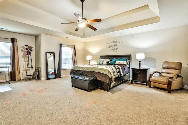 bedroom featuring ceiling fan, light colored carpet, a tray ceiling, and multiple windows