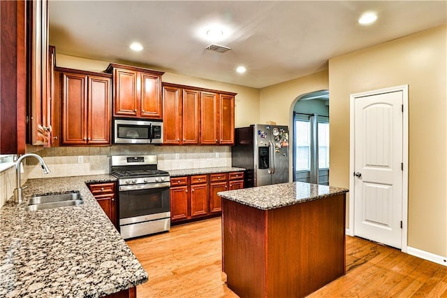 kitchen with sink, a center island, light stone counters, stainless steel appliances, and light wood-type flooring