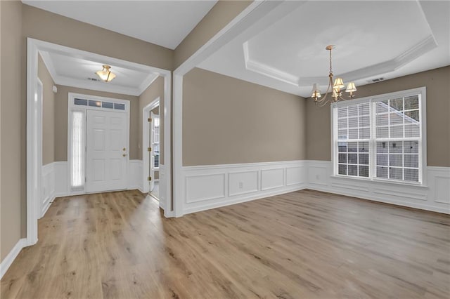 entryway with a tray ceiling, light hardwood / wood-style floors, and an inviting chandelier