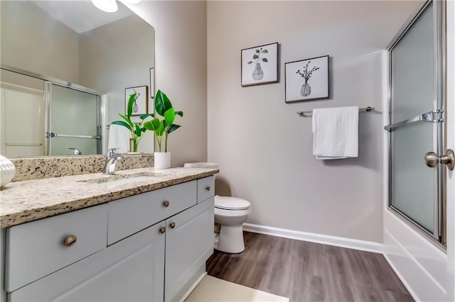 bathroom with shower / bath combination with glass door, toilet, vanity, wood finished floors, and baseboards