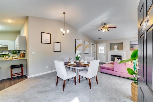 carpeted dining room featuring lofted ceiling, a glass covered fireplace, baseboards, and ceiling fan with notable chandelier