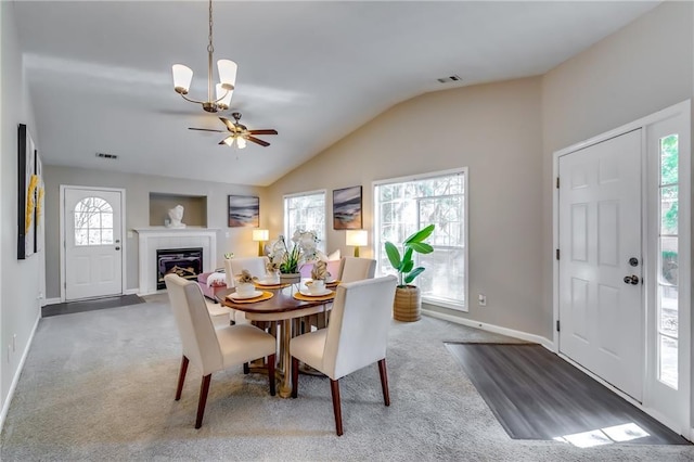 carpeted dining room featuring lofted ceiling, a fireplace with flush hearth, visible vents, and baseboards