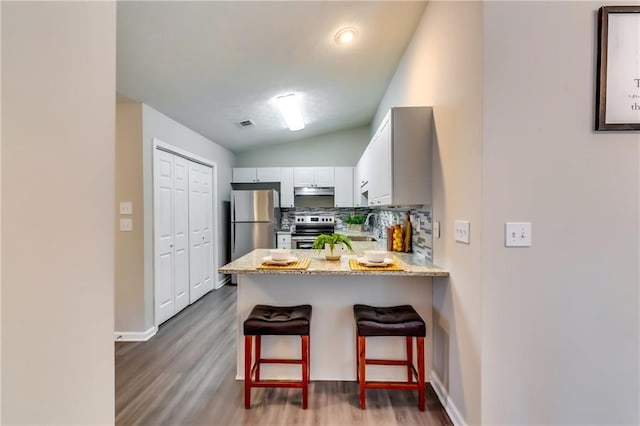 kitchen with stainless steel appliances, backsplash, white cabinets, vaulted ceiling, and a peninsula