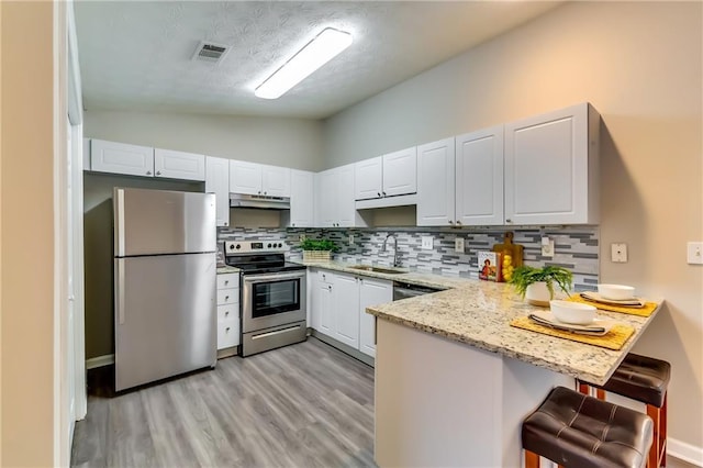 kitchen with stainless steel appliances, visible vents, a sink, a peninsula, and under cabinet range hood