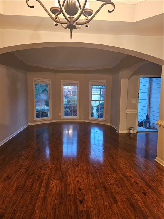 unfurnished living room with dark hardwood / wood-style floors, crown molding, and an inviting chandelier