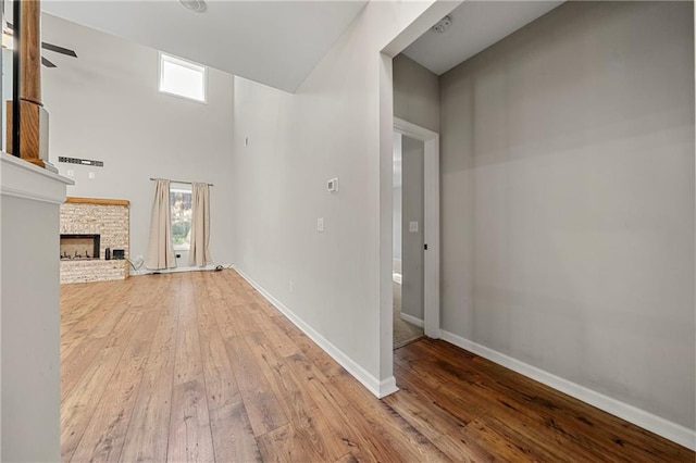 unfurnished living room with ceiling fan, a towering ceiling, a fireplace, and light wood-type flooring