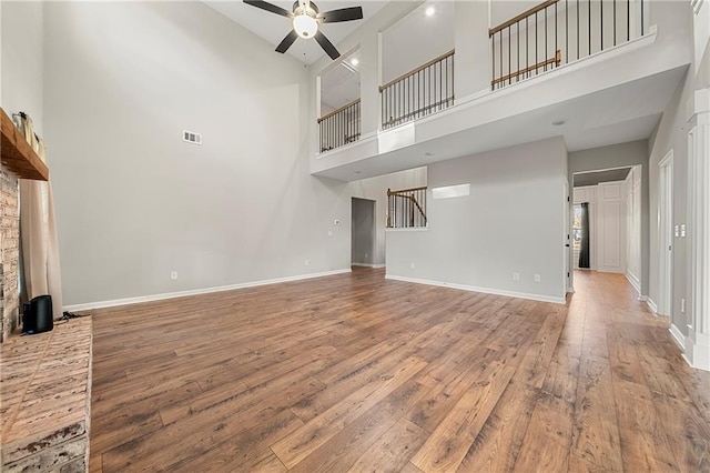 unfurnished living room featuring a towering ceiling, hardwood / wood-style floors, and ceiling fan