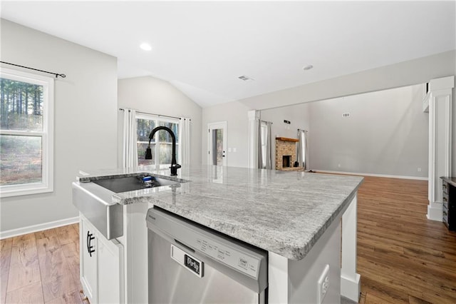 kitchen featuring a kitchen island with sink, a brick fireplace, stainless steel dishwasher, and white cabinets