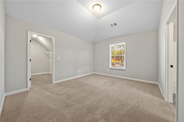 unfurnished bedroom featuring a walk in closet, lofted ceiling, a closet, and light carpet