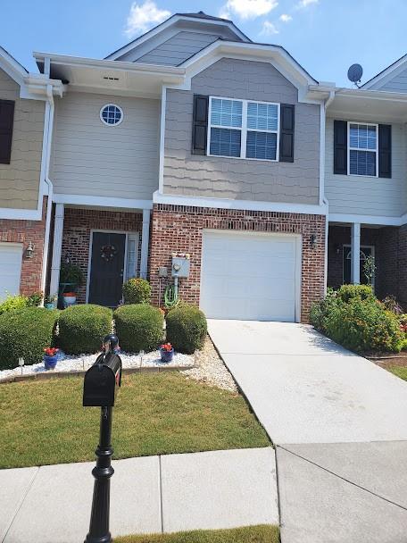 view of property with an attached garage, concrete driveway, a front yard, and brick siding