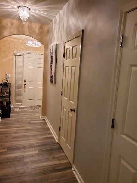 corridor with baseboards, wood finished floors, and a chandelier
