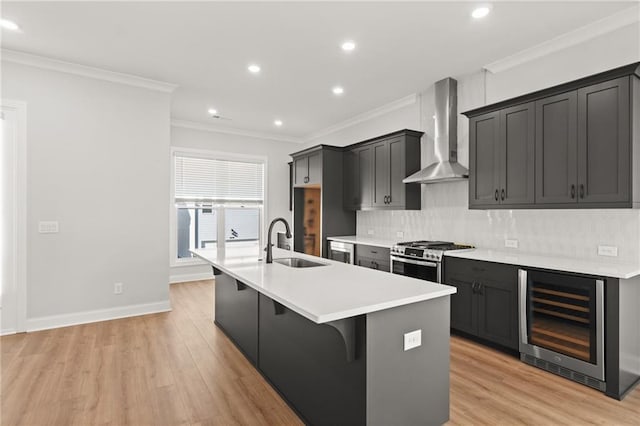 kitchen featuring sink, a kitchen island with sink, wine cooler, stainless steel range with gas cooktop, and wall chimney exhaust hood