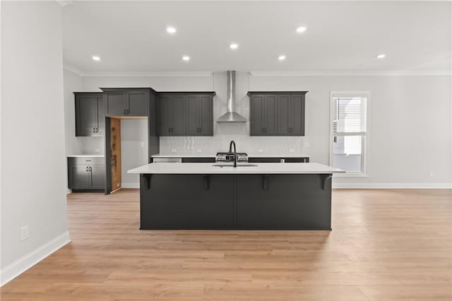 kitchen featuring crown molding, light hardwood / wood-style floors, a kitchen island with sink, and wall chimney range hood