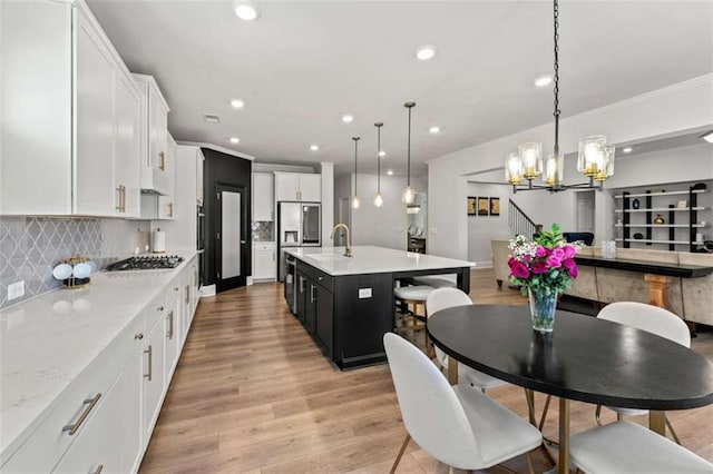 kitchen with light wood-style flooring, stainless steel appliances, a sink, white cabinets, and tasteful backsplash