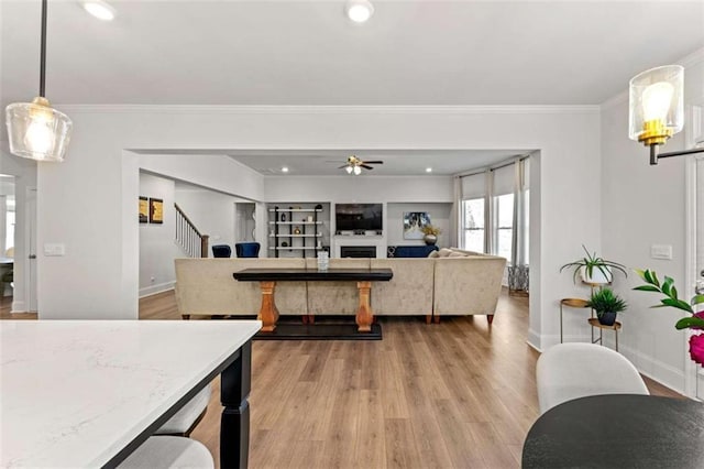 dining room featuring light wood-style floors, ceiling fan, a fireplace, and crown molding