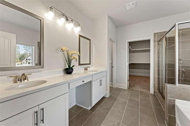 full bathroom featuring double vanity, a spacious closet, a stall shower, and a sink