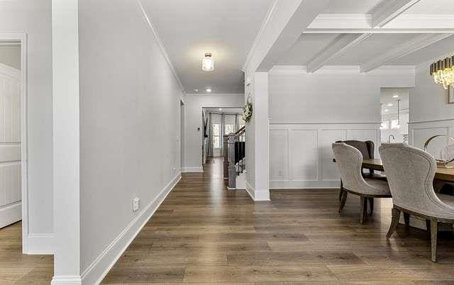 hall featuring beam ceiling, a decorative wall, wood finished floors, and crown molding