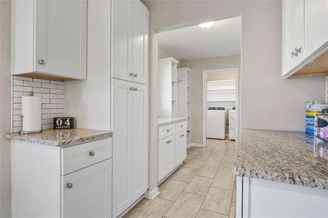 kitchen featuring white cabinets, washing machine and clothes dryer, light stone counters, and tasteful backsplash