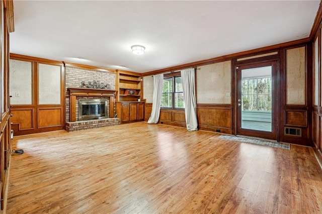 unfurnished living room featuring wood walls, light hardwood / wood-style floors, built in features, and a brick fireplace