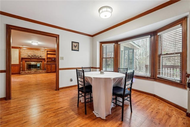 dining space with light wood-type flooring, a brick fireplace, and crown molding