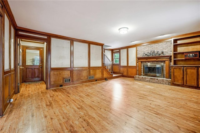 unfurnished living room with crown molding, wooden walls, built in shelves, a fireplace, and light hardwood / wood-style floors