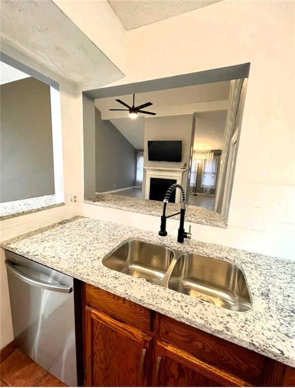 kitchen with ceiling fan, a fireplace, a sink, light stone countertops, and dishwasher