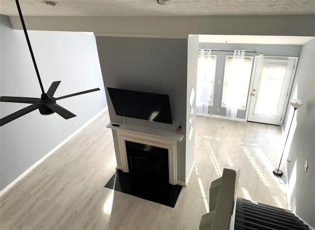 living room featuring light wood-style floors, a ceiling fan, baseboards, and a textured ceiling