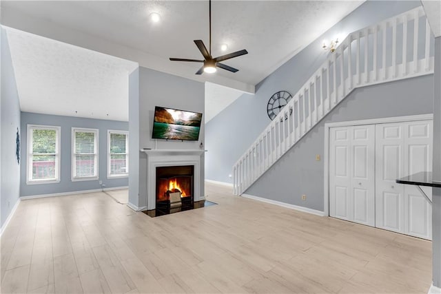 unfurnished living room with stairway, light wood-type flooring, a fireplace with flush hearth, and a ceiling fan