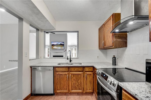 kitchen featuring wall chimney range hood, appliances with stainless steel finishes, brown cabinetry, and a sink