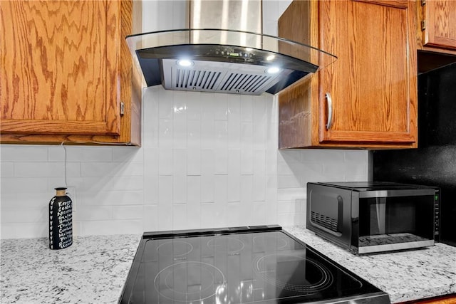 kitchen featuring brown cabinets, decorative backsplash, island exhaust hood, and light stone countertops