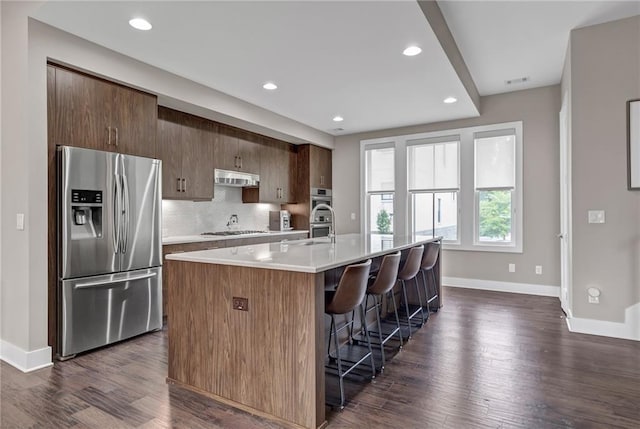 kitchen featuring a breakfast bar area, dark hardwood / wood-style flooring, an island with sink, stainless steel appliances, and backsplash