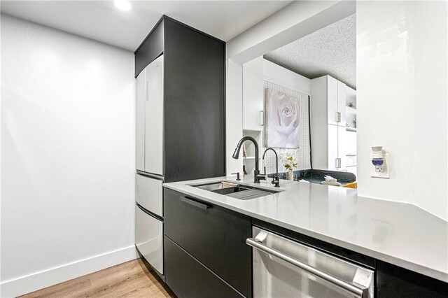 kitchen with light wood-type flooring, a textured ceiling, sink, white cabinets, and stainless steel dishwasher