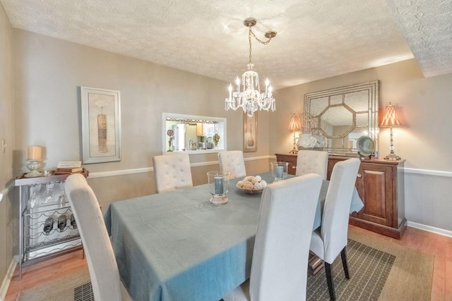 dining area with light wood finished floors, a chandelier, a textured ceiling, and baseboards