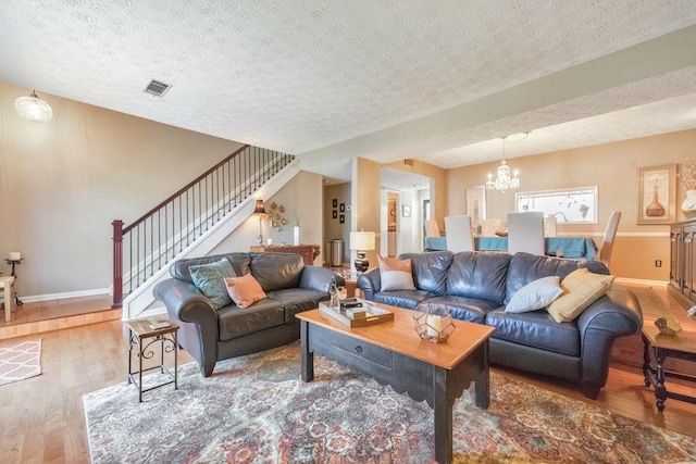 living area featuring visible vents, a notable chandelier, wood finished floors, baseboards, and stairs