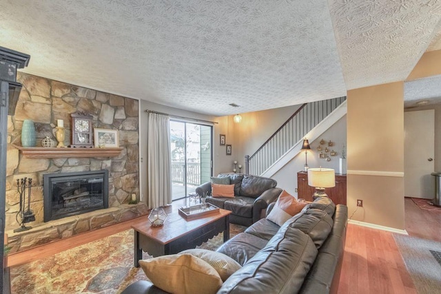 living room featuring a stone fireplace, stairs, wood finished floors, and a textured ceiling