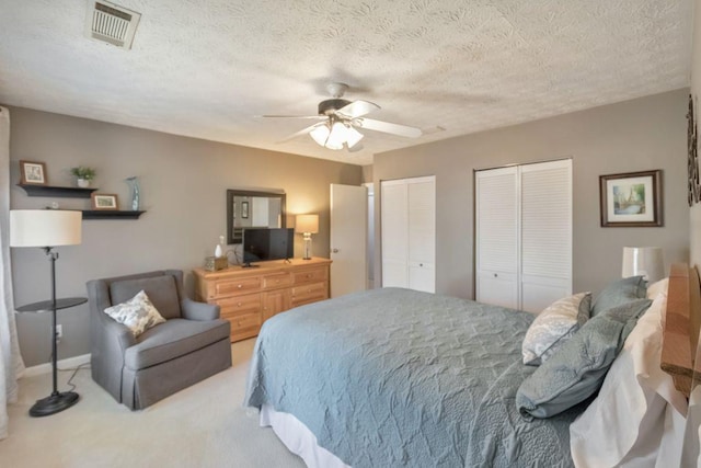 carpeted bedroom with visible vents, a textured ceiling, two closets, and ceiling fan