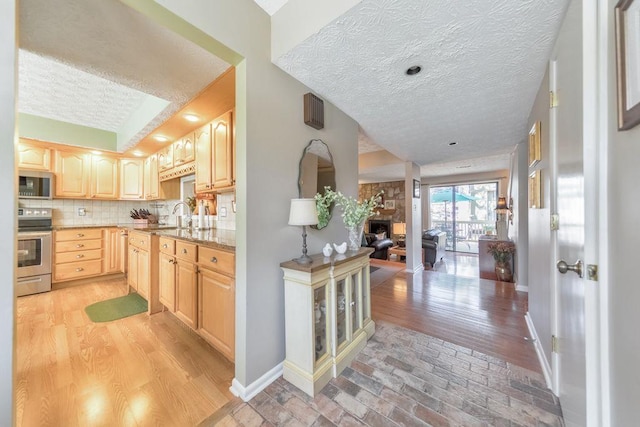 kitchen with tasteful backsplash, light brown cabinets, baseboards, open floor plan, and appliances with stainless steel finishes