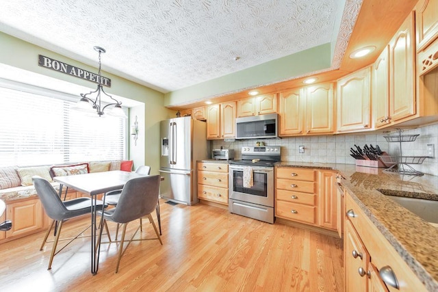 kitchen featuring tasteful backsplash, light brown cabinets, light wood-style floors, and stainless steel appliances