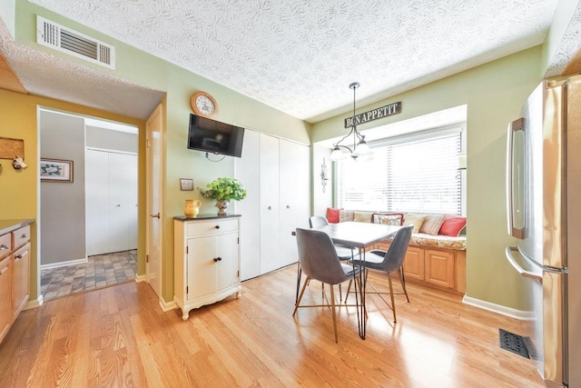 dining area with light wood-style flooring, visible vents, and a textured ceiling