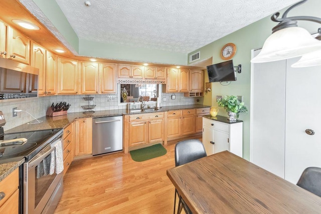 kitchen with a sink, decorative backsplash, stainless steel appliances, a textured ceiling, and light wood-type flooring