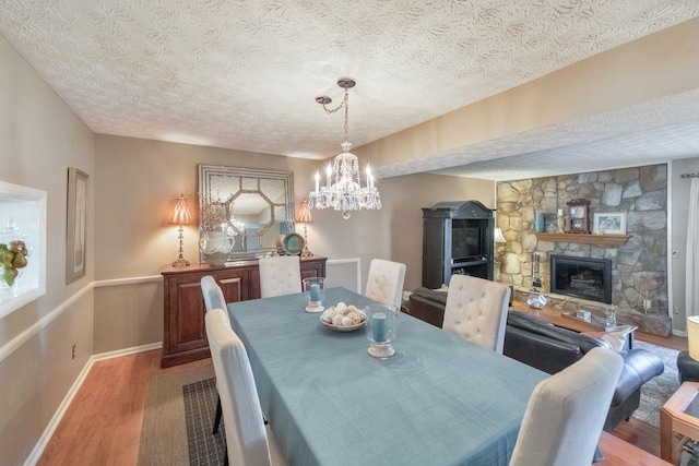 dining space featuring a fireplace, wood finished floors, baseboards, and a textured ceiling