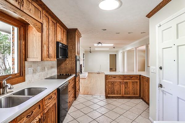 kitchen with black appliances, light tile patterned floors, brown cabinetry, and a sink