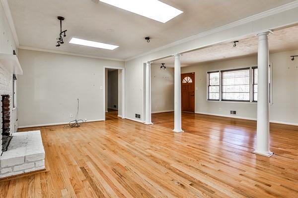 unfurnished living room with crown molding, a fireplace with raised hearth, decorative columns, and wood finished floors