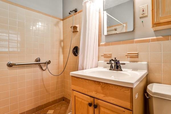 full bath with tiled shower, tile walls, toilet, and vanity