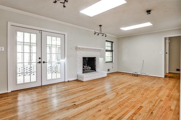 unfurnished living room with light wood-type flooring, french doors, crown molding, and a brick fireplace